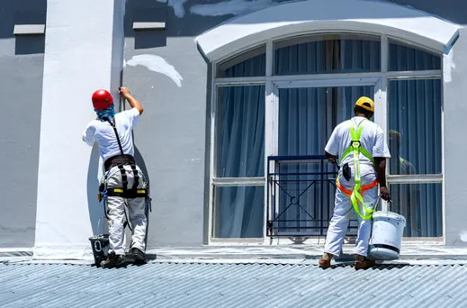 Two harnessed painters working on an apartment exterior in the South Bay
